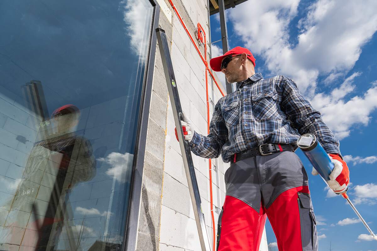 worker applies sealant to a building window during Y4XNKD8